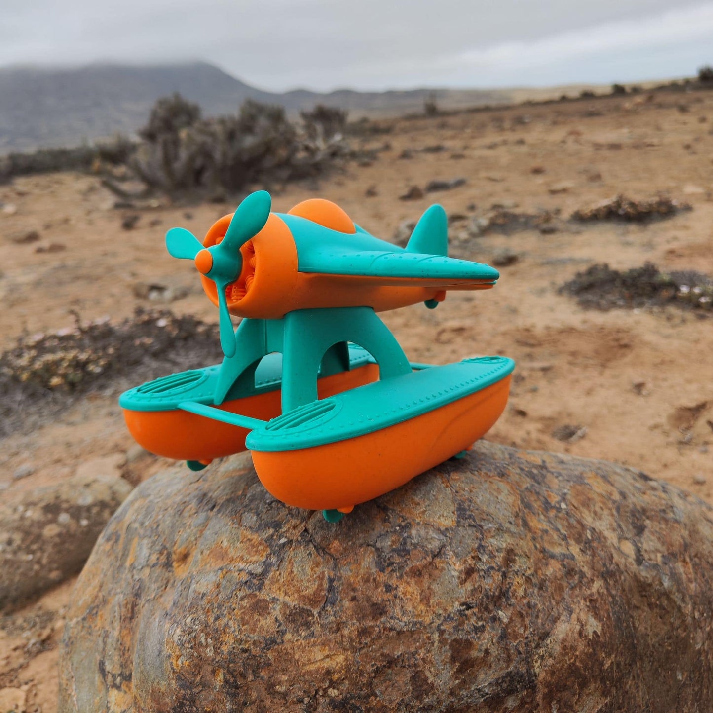 Hidroavión eco-friendly de paja de trigo que flota, color anaranjado y calipso, en un escenario desértico
