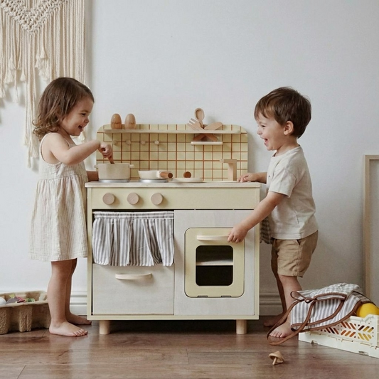Niño y niña jugando juego de rol con la cocina de madera montessori estilo vintage, que incluye sus accesorios (olla, sartén, utencilios, salero y pimentero)