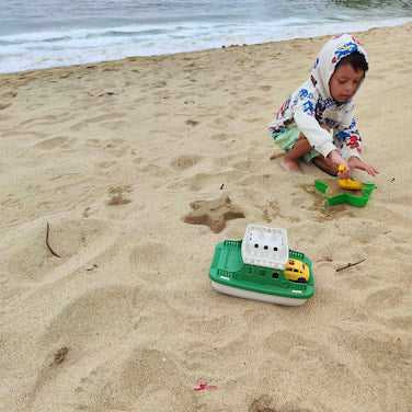 Niño jugando en la arena de la playa con el ferry eco-friendly con rampa y carritos