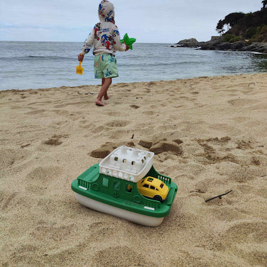 Niño jugando en la arena de la playa con el ferry eco-friendly con rampa y carritos