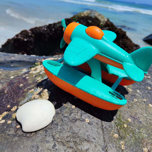 Hidroavión eco-friendly de paja de trigo que flota, color anaranjado y calipso, en un escenario natural de playa