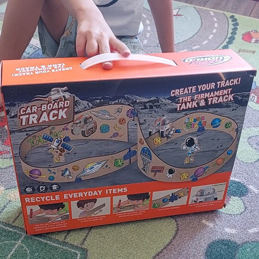 Niño mostrando pista espacial DIY en cartón reciclable con vehículo incluido  en su empaque