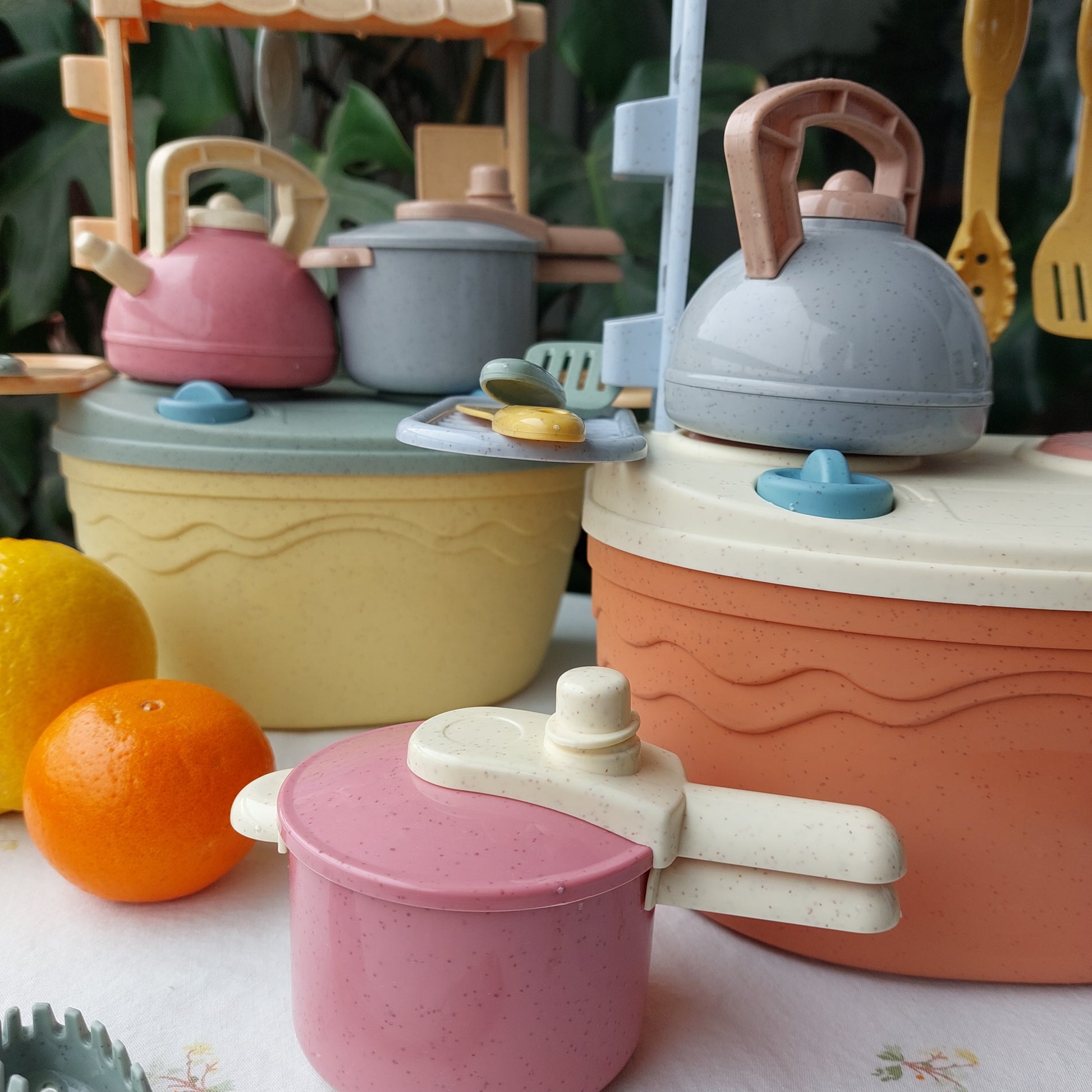 Set de cocina portátil de bioplástico de paja de trigo en dos colores (coral claro y amarillo). Incluye hornilla, utensilios tetera y olla a presión. La hornilla funciona como caja de almacenamiento del juguete